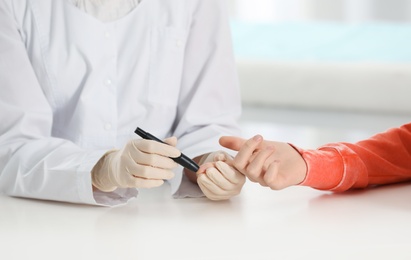 Doctor taking patient's blood sample with lancet pen in hospital, closeup. Diabetes control