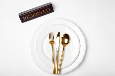 Elegant table setting with RESERVED sign on white background, top view