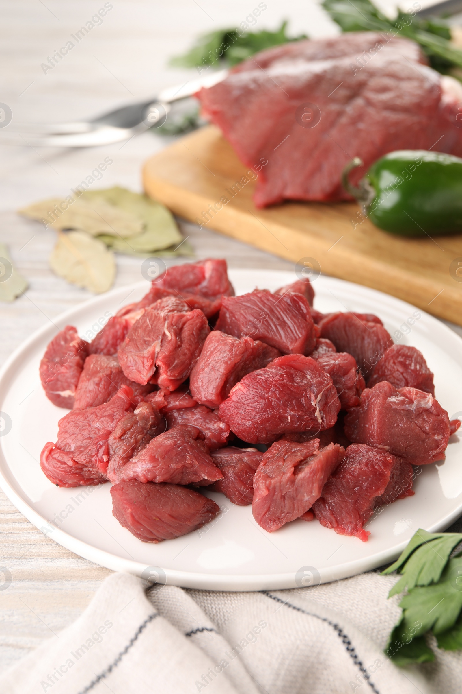 Photo of Plate with pieces of raw beef meat on light wooden table