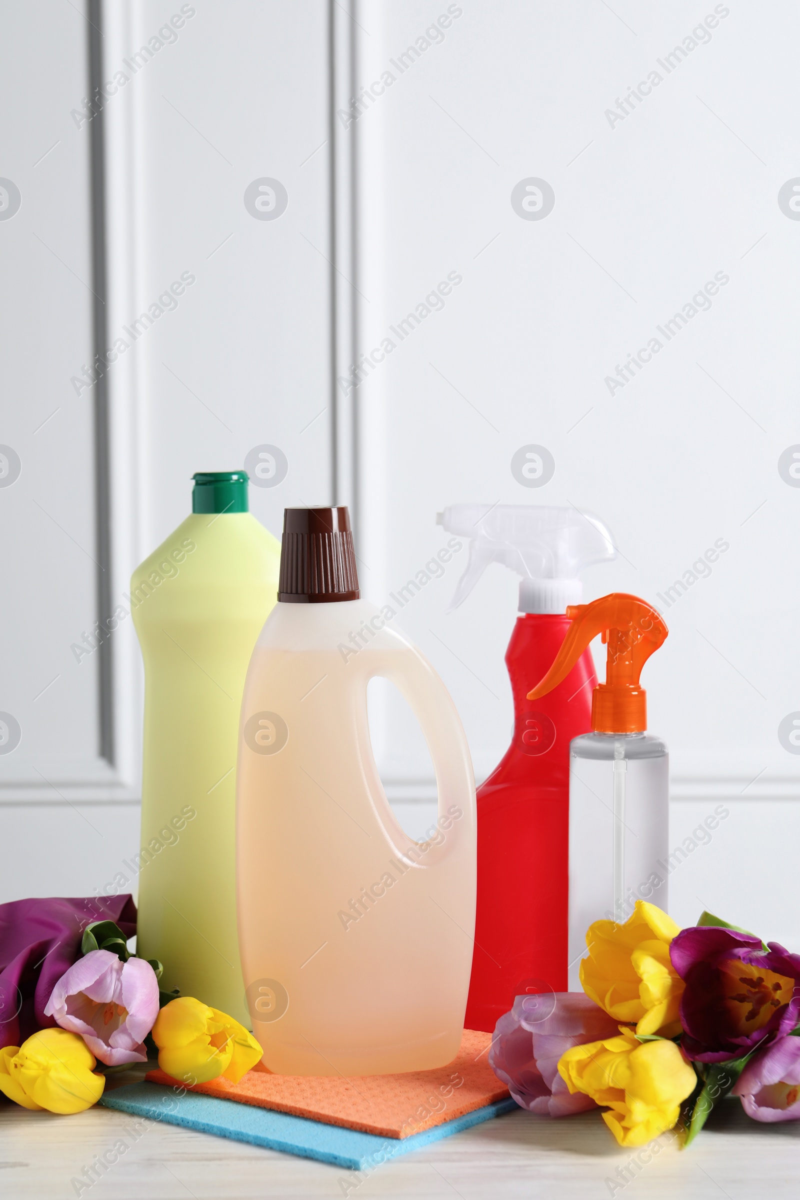 Photo of Spring cleaning. Detergents, flowers and rags on white wooden table