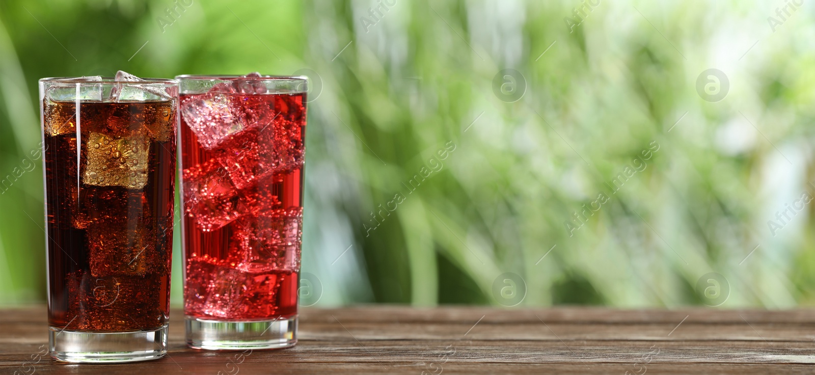 Image of Tasty refreshing soda drinks with ice cubes on wooden table outdoors. Banner design with space for text