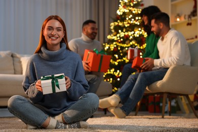 Photo of Christmas celebration in circle of friends. Happy young woman with gift box at home, selective focus