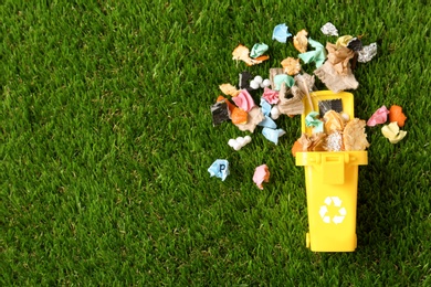 Photo of Trash bin and different garbage on green grass, top view with space for text. Waste recycling concept