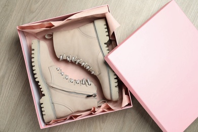 Pair of stylish boots in box on wooden background, top view