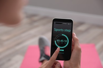 Photo of Young woman using fitness app on smartphone indoors, closeup