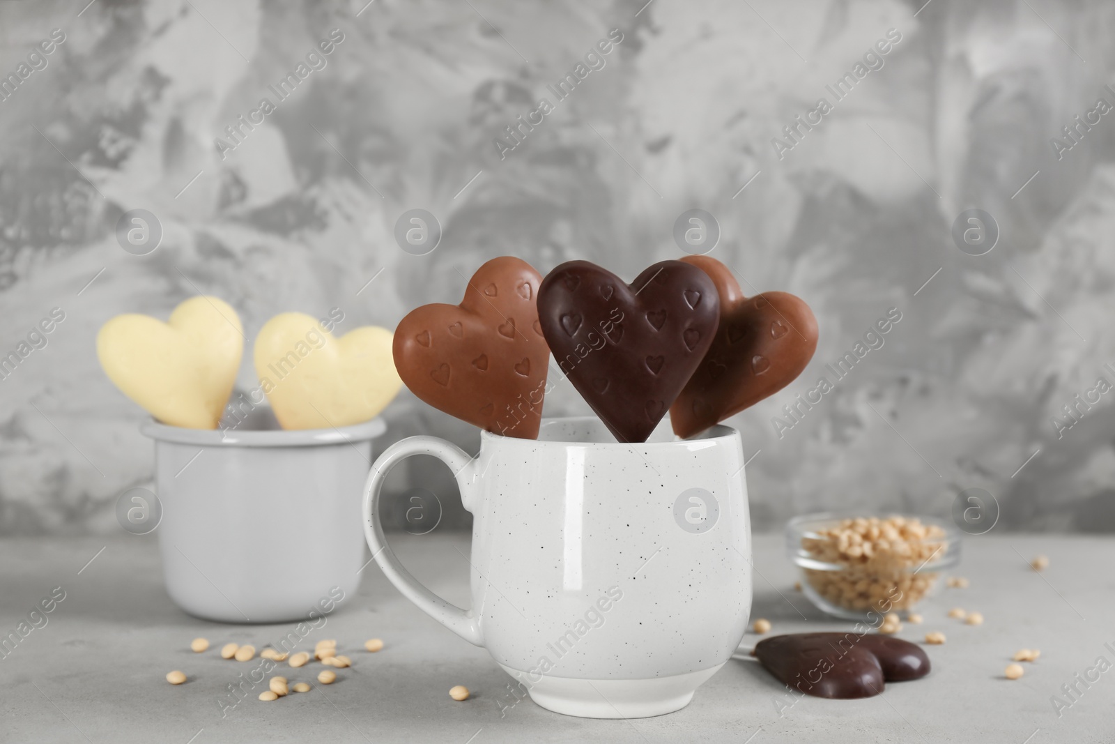 Photo of Heart shaped lollipops made of chocolate in cups on grey table