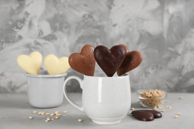 Heart shaped lollipops made of chocolate in cups on grey table