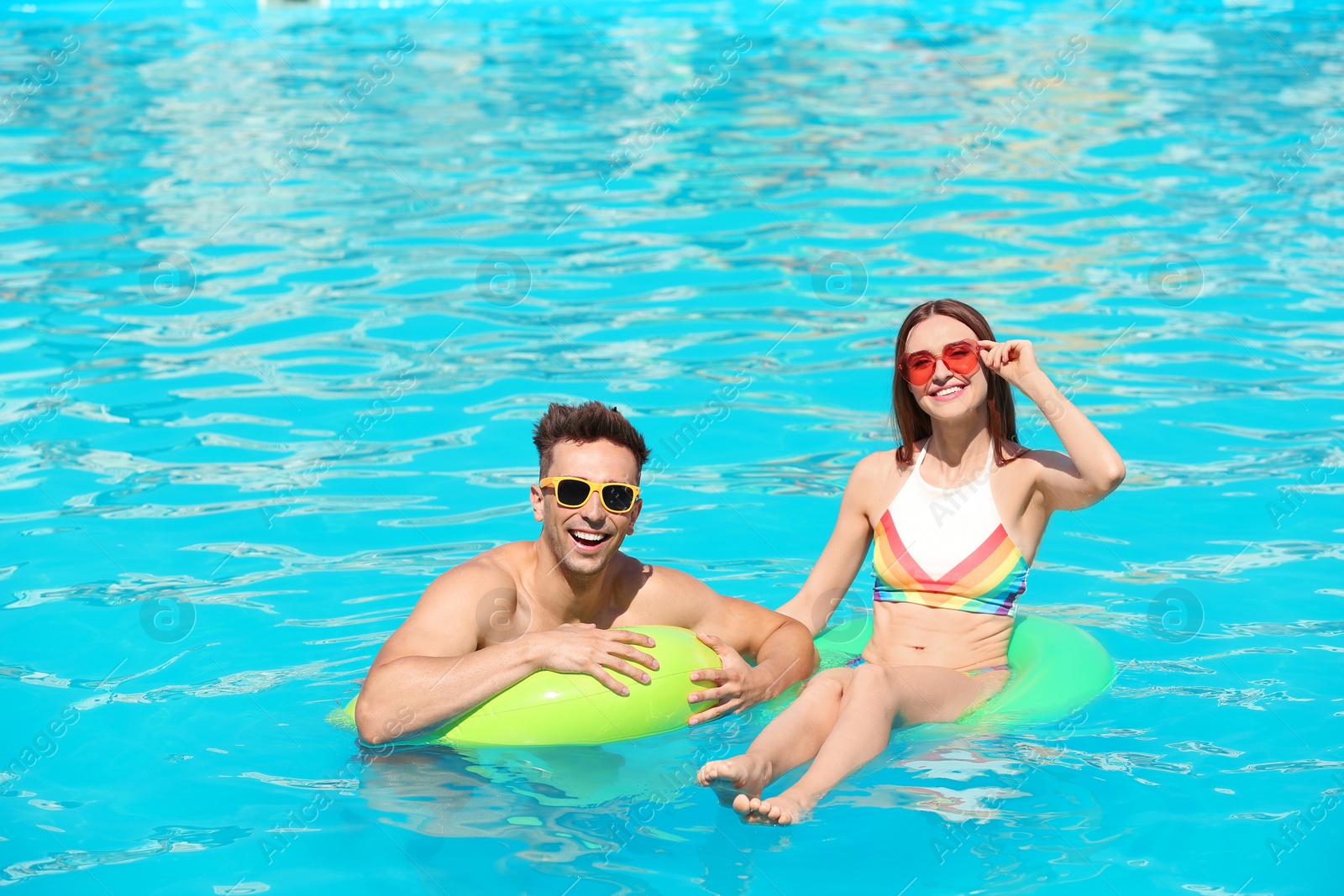 Photo of Happy young couple with inflatable rings in swimming pool