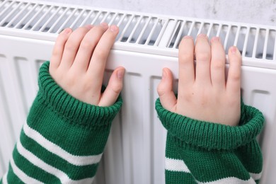 Photo of Girl warming hands on heating radiator, closeup