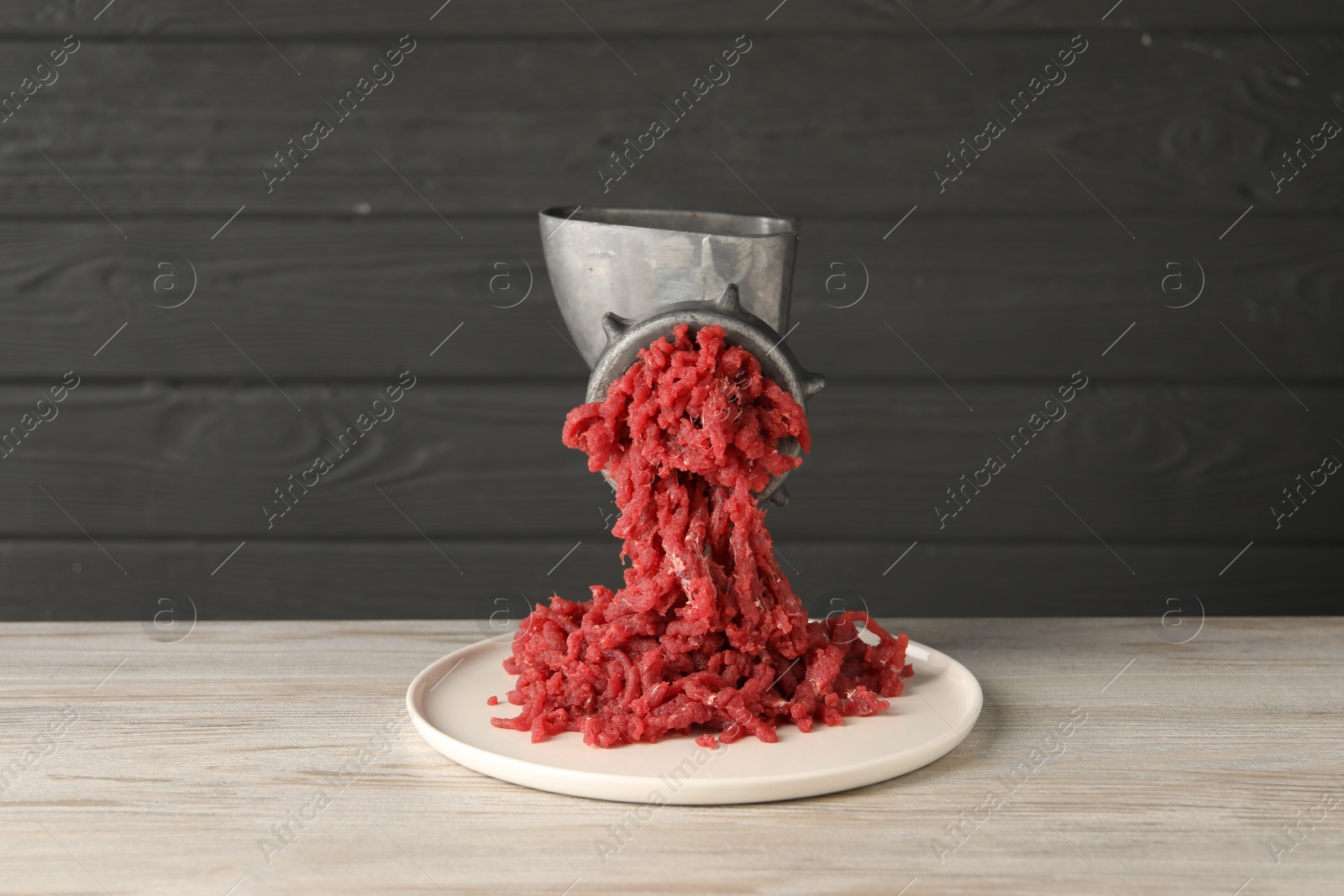 Photo of Metal meat grinder with beef mince on light wooden table