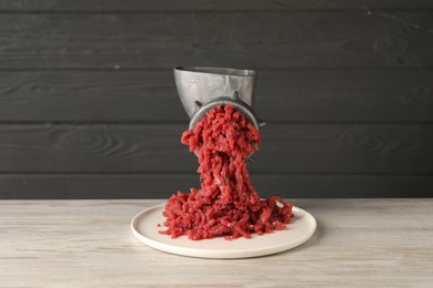 Metal meat grinder with beef mince on light wooden table