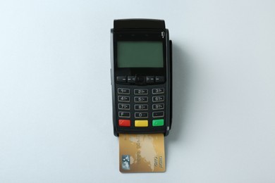 New modern payment terminal with credit card on light background, top view