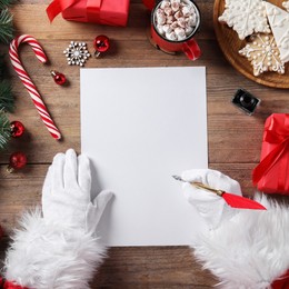 Photo of Santa Claus with letter, feather and Christmas decor at wooden table, top view. Space for text