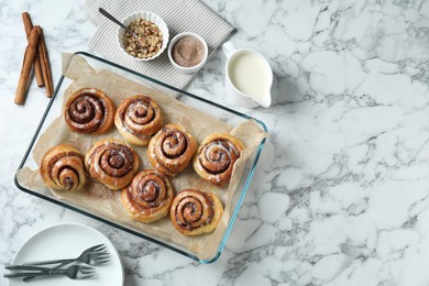 Photo of Tasty cinnamon rolls in baking dish served on white marble table, flat lay. Space for text