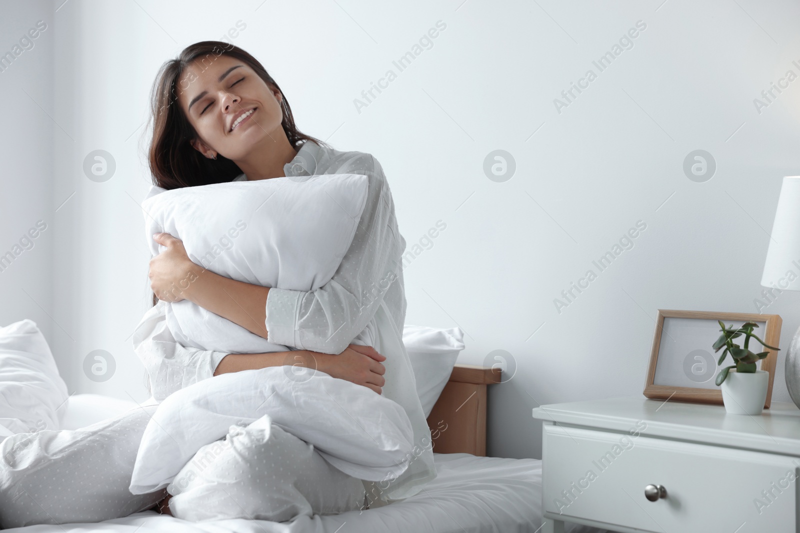 Photo of Beautiful young woman hugging pillow on bed at home