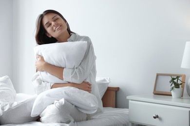 Beautiful young woman hugging pillow on bed at home