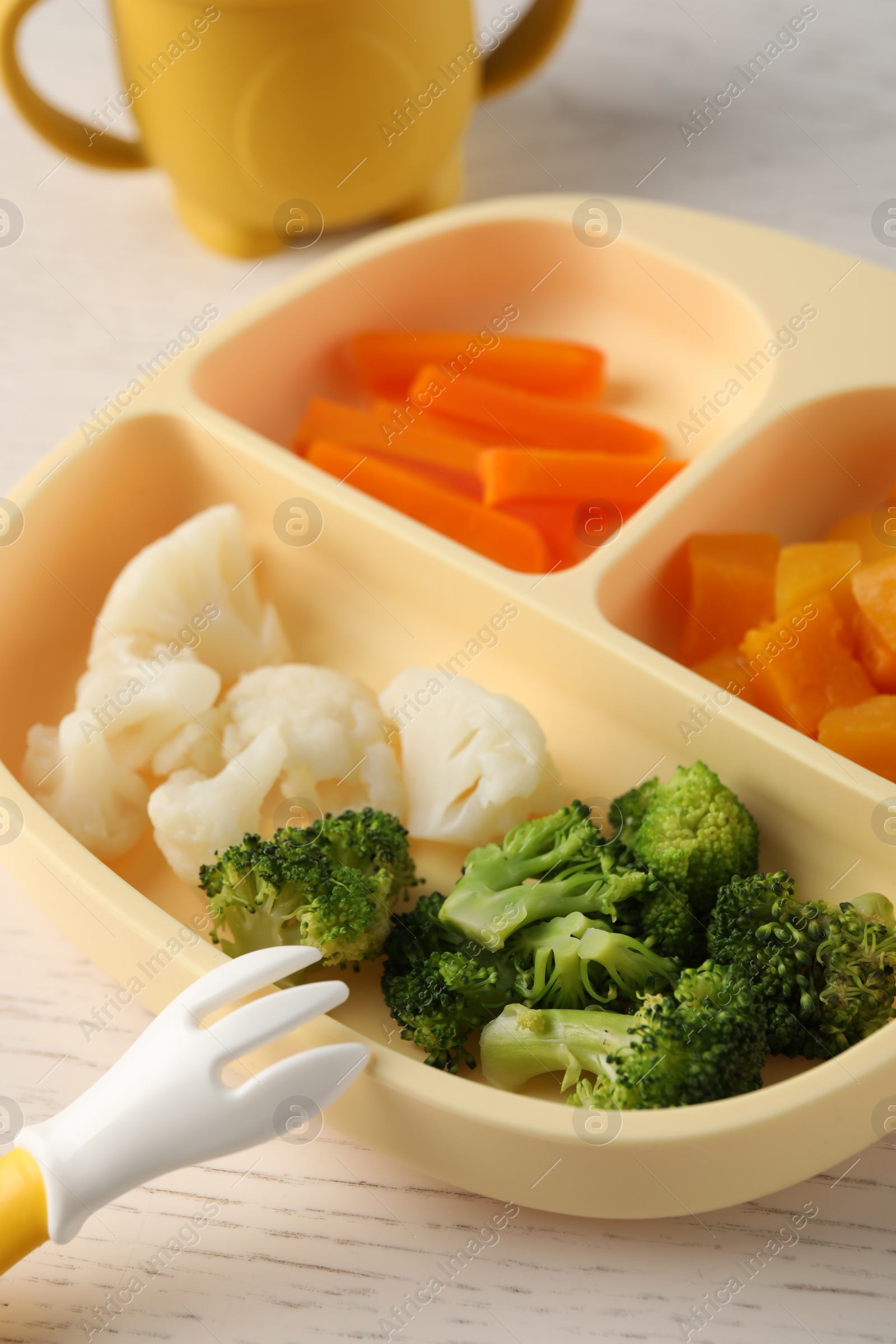 Photo of Baby food. Section plate with different vegetables on white wooden table, closeup