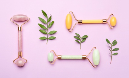 Photo of Natural face rollers and leaves on pink background, flat lay