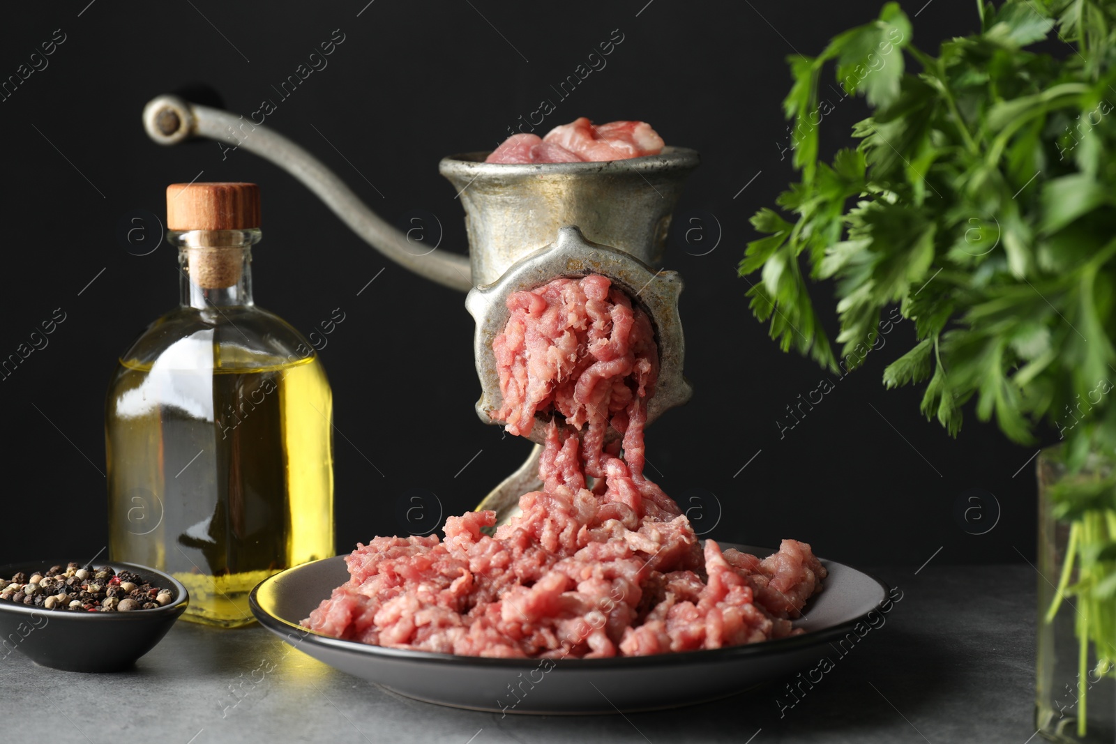 Photo of Manual meat grinder with beef mince, spices, oil and parsley on grey table