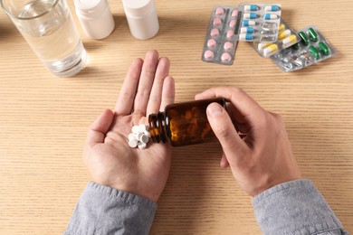 Man pouring pills from bottle onto hand at wooden table, top view