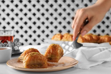 Photo of Woman serving delicious sweet baklava at white table, closeup