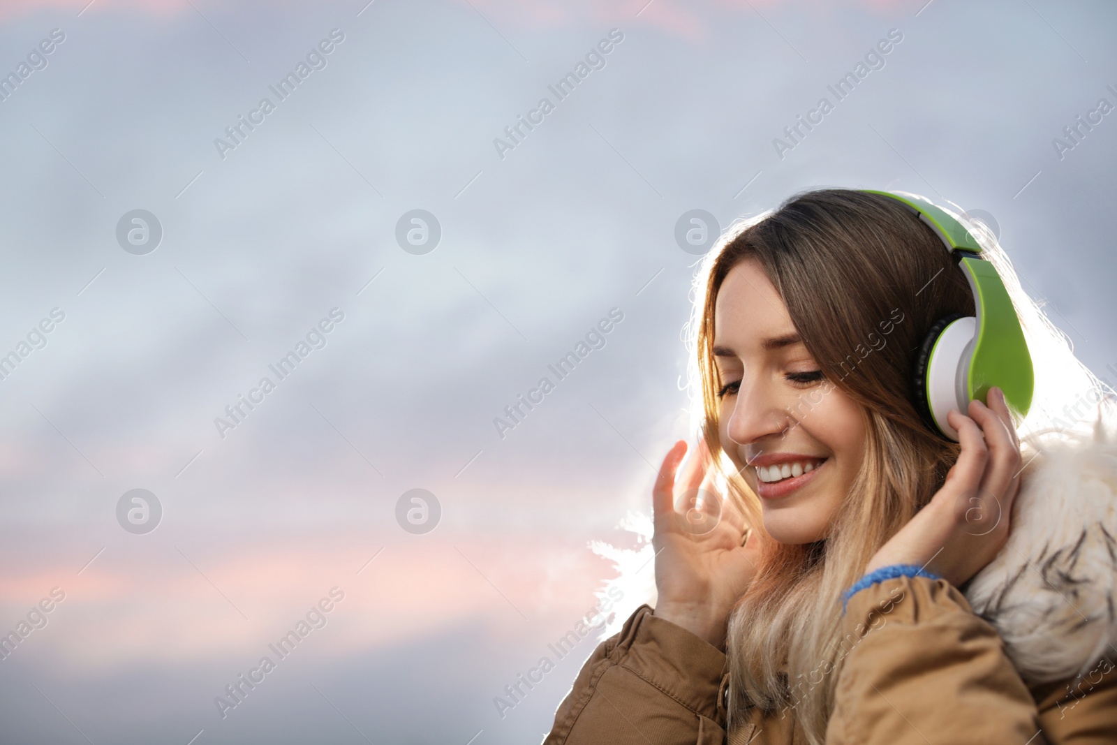 Photo of Young woman with headphones listening to music outdoors, space for text