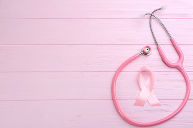 Photo of Pink ribbon and stethoscope on wooden background, flat lay with space for text. Breast cancer concept
