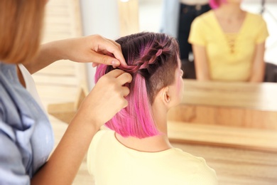 Photo of Professional stylist braiding woman's color hair in beauty salon. Modern trend