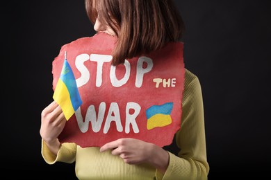 Photo of Woman holding poster with words Stop the War and Ukrainian flag on black background