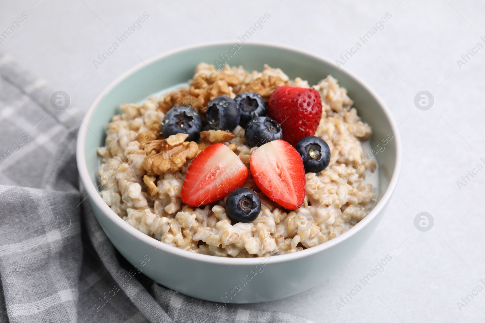 Photo of Tasty oatmeal with strawberries, blueberries and walnuts in bowl on grey table