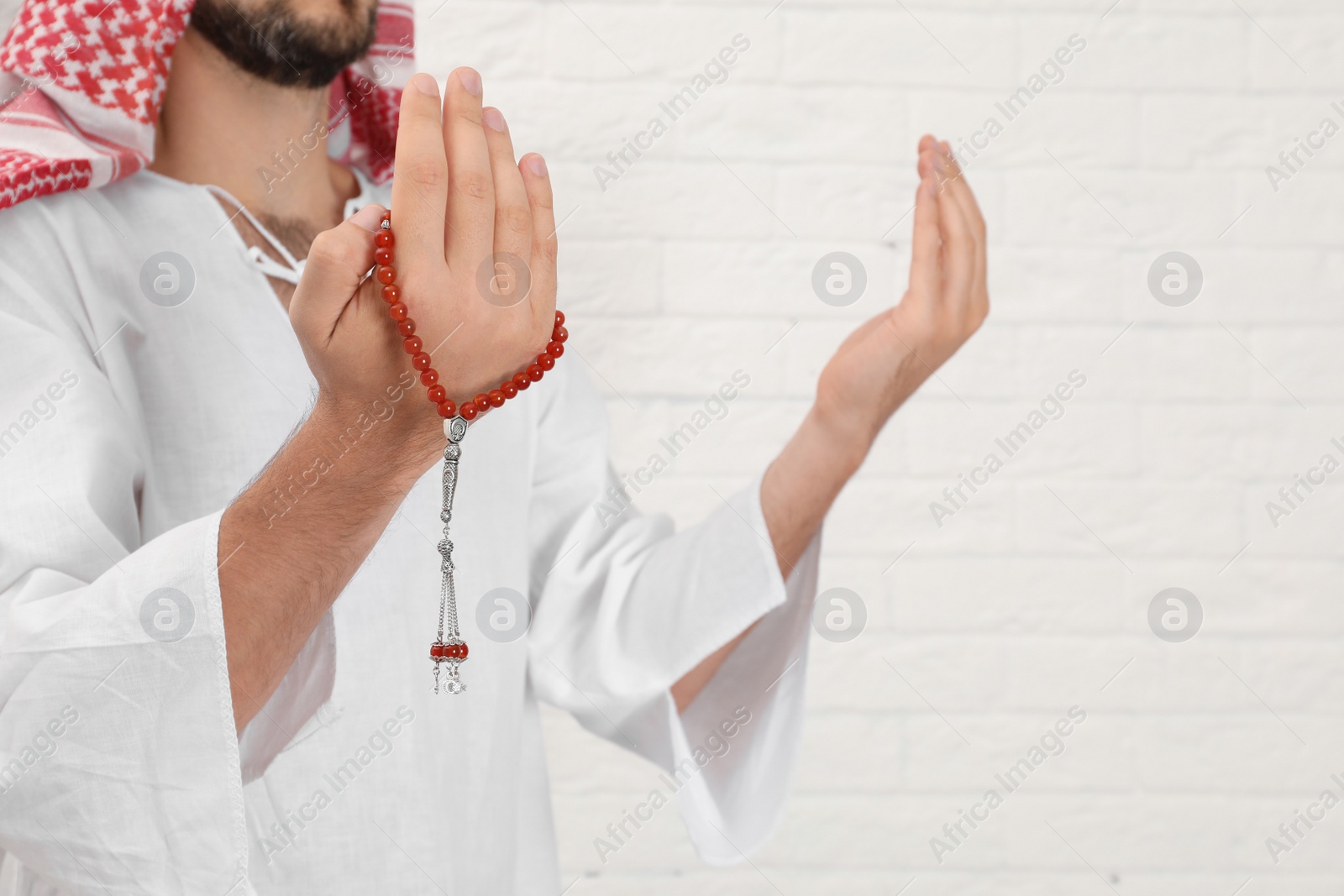 Photo of Muslim man praying near brick wall, closeup