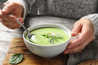 Photo of Woman eating fresh vegetable detox soup made of green peas at table, closeup