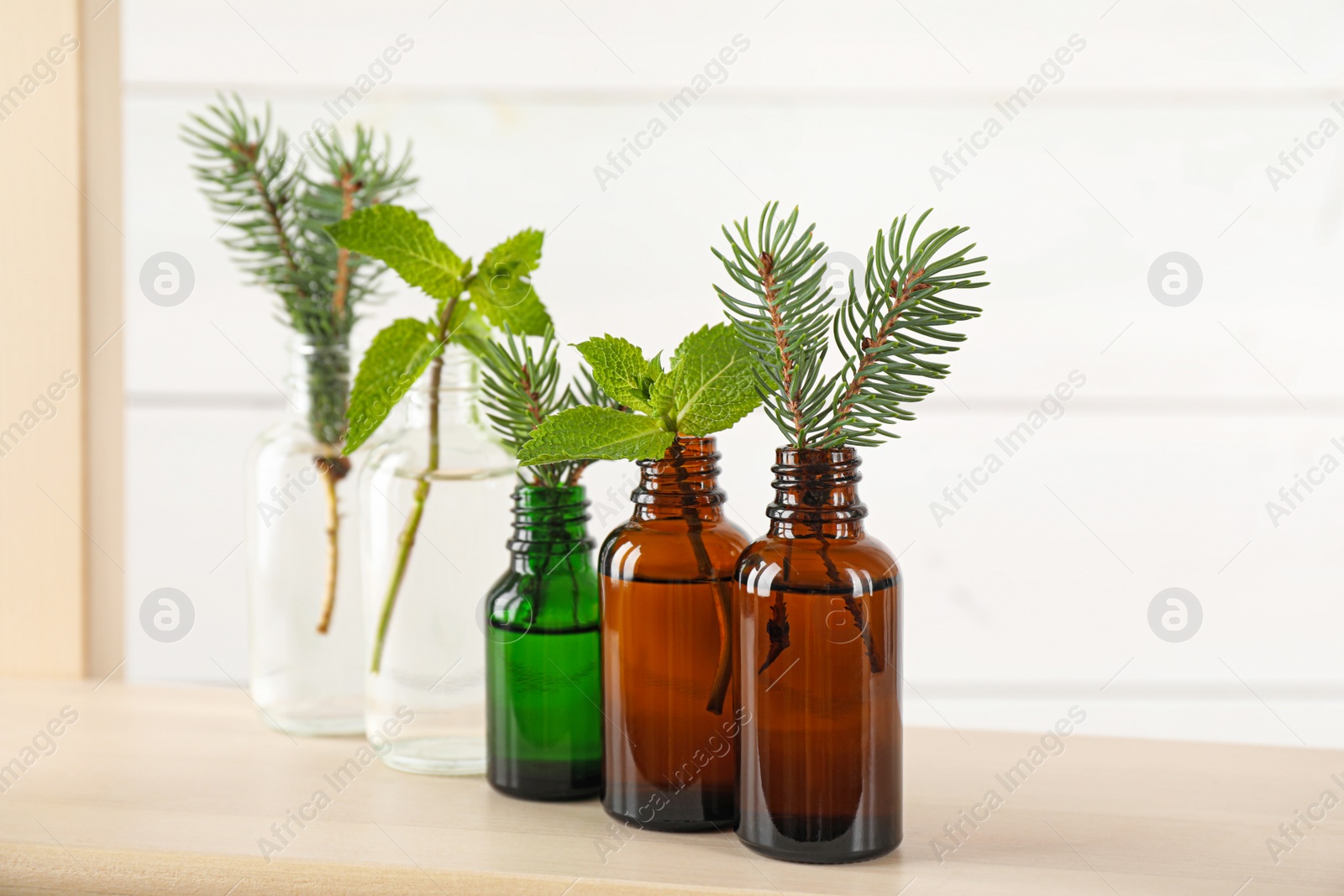 Photo of Glass bottles of different essential oils with plants on table