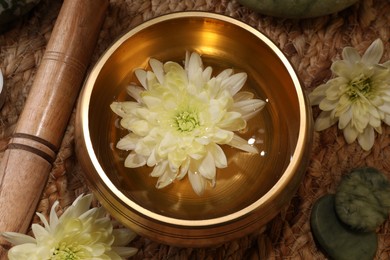 Photo of Tibetan singing bowl with water, beautiful chrysanthemum flowers, mallet and stones on table, flat lay