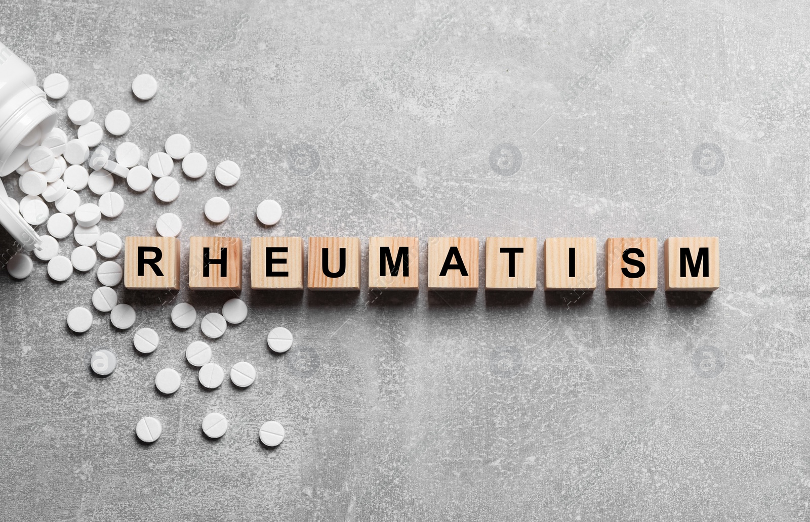 Photo of Word Rheumatism made of cubes and pills on light gray textured background, flat lay