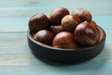 Photo of Roasted edible sweet chestnuts on light blue wooden table, closeup