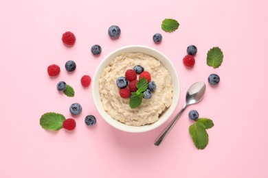 Photo of Tasty oatmeal porridge with raspberries and blueberries in bowl on pink background, flat lay