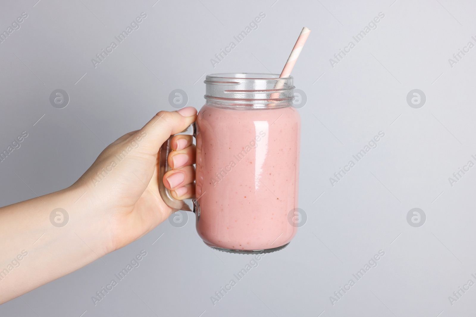 Photo of Woman holding mason jar of tasty smoothie on light grey background, closeup