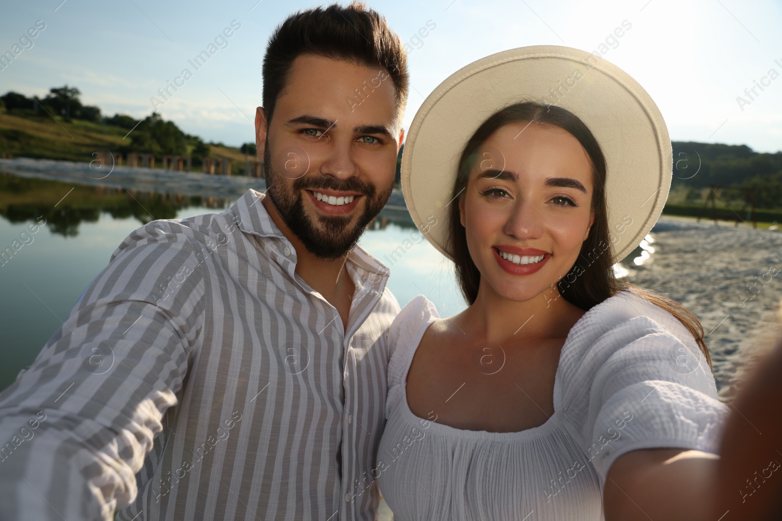 Photo of Romantic date. Beautiful couple making selfie near lake on sunny day