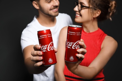 Photo of MYKOLAIV, UKRAINE - NOVEMBER 28, 2018: Young couple with Coca-Cola cans on dark background