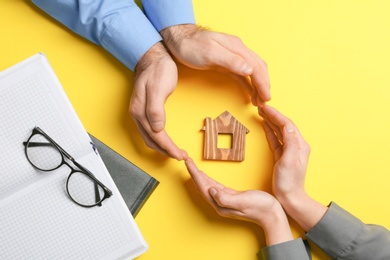 Photo of Couple holding hands near figure of house on color background, top view. Home insurance