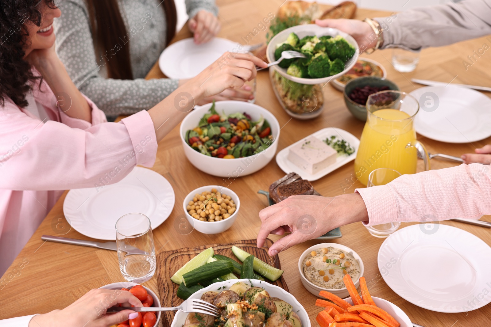 Photo of Friends eating vegetarian food at wooden table indoors, closeup