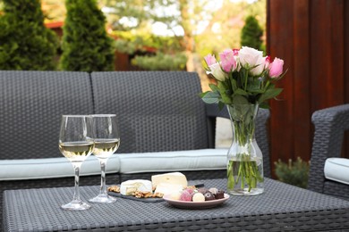 Vase with roses, glasses of wine and food on rattan table on outdoor terrace