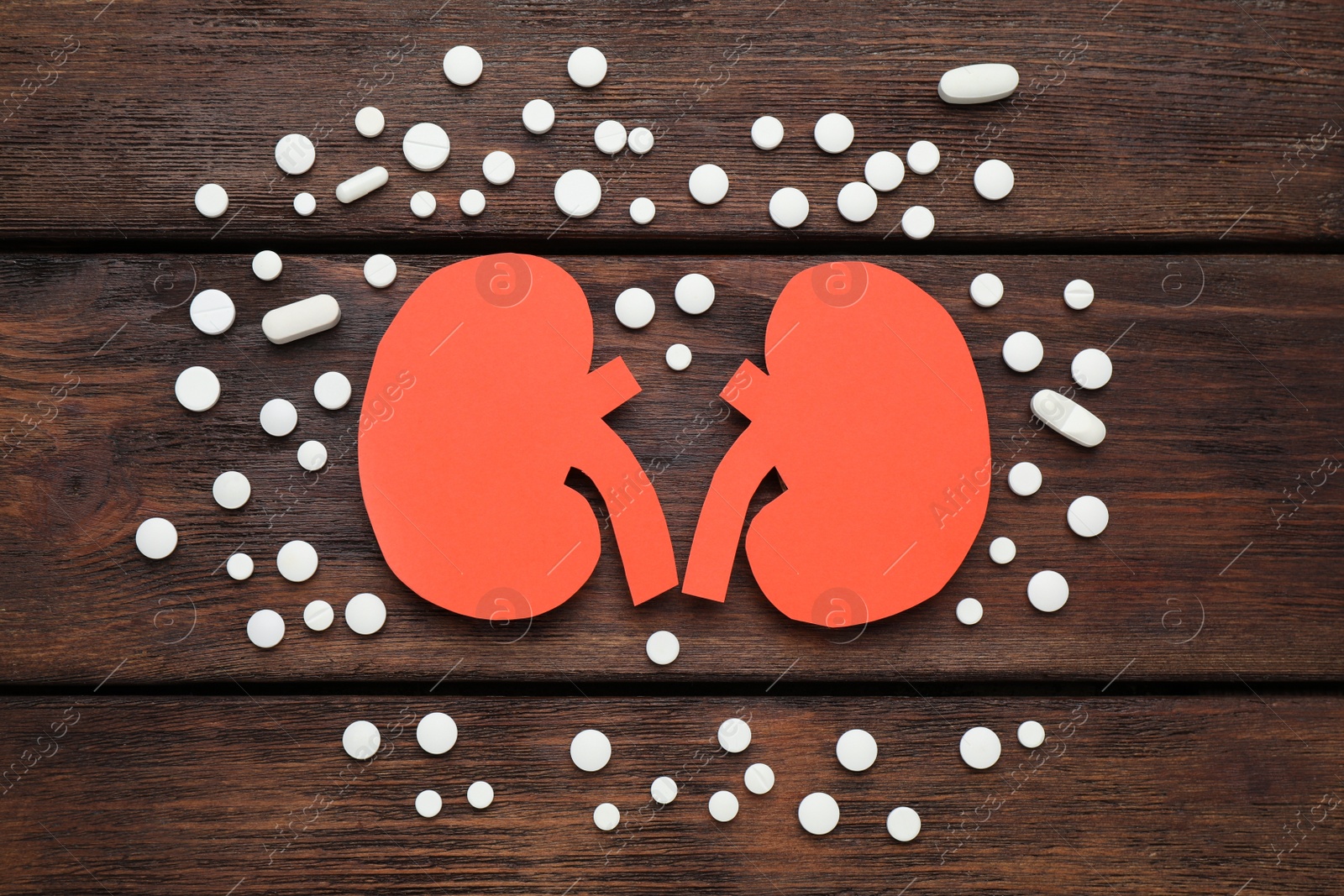 Photo of Paper cutout of kidneys and pills on wooden table, flat lay