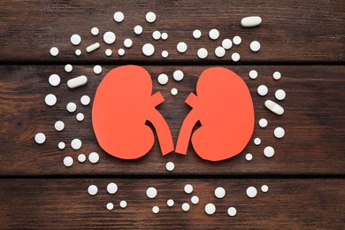 Paper cutout of kidneys and pills on wooden table, flat lay