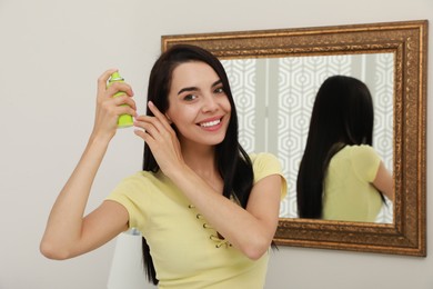 Photo of Woman applying dry shampoo onto her hair near mirror