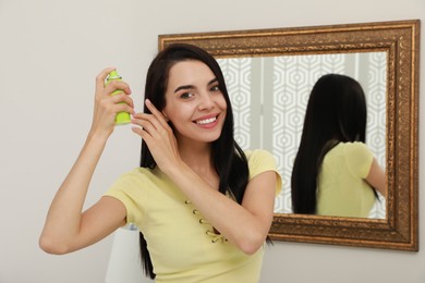 Woman applying dry shampoo onto her hair near mirror