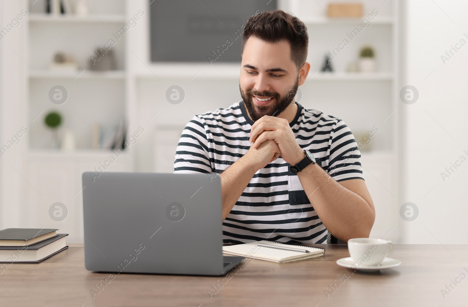 Photo of Young man watching webinar at table in room