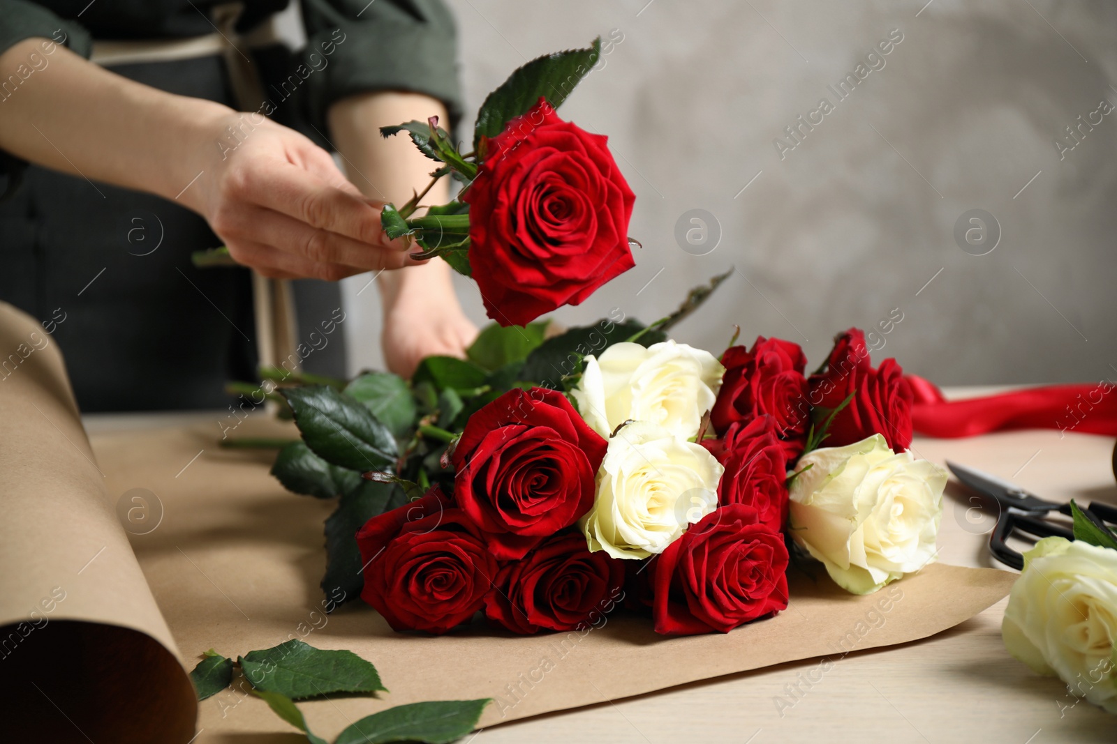 Photo of Woman making luxury bouquet of fresh roses at wooden table, closeup