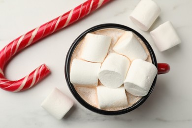 Photo of Tasty hot chocolate with marshmallows and candy cane on white marble table, top view